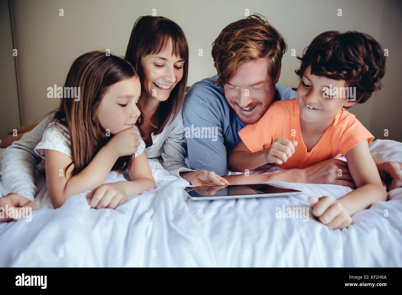 I bambini e i loro genitori guardando il tablet sul letto Foto Stock