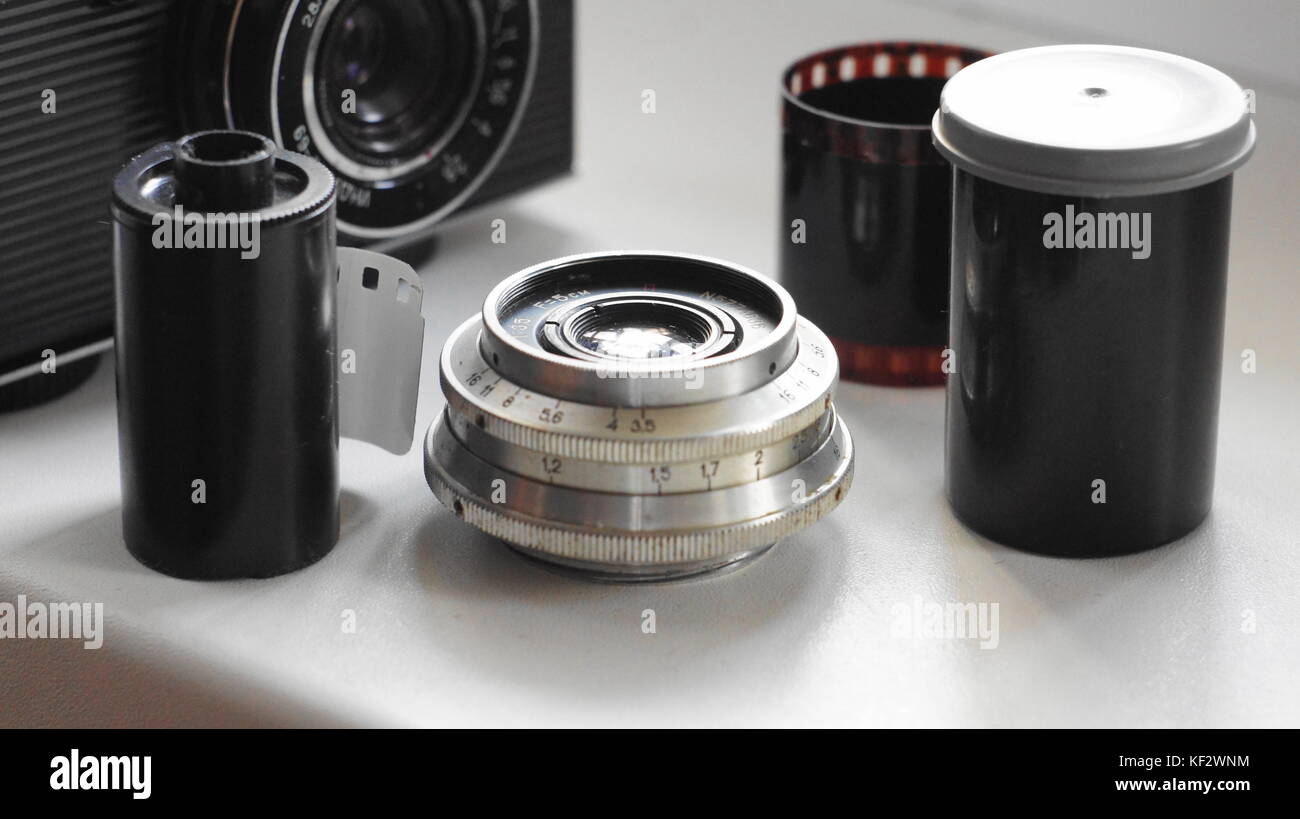 Ancora una vita di accessori da vecchi film fotocamera: telecamera, obiettivo, cassetta delle pellicole e un pezzo di pellicola, contenitore di pellicola. Foto Stock