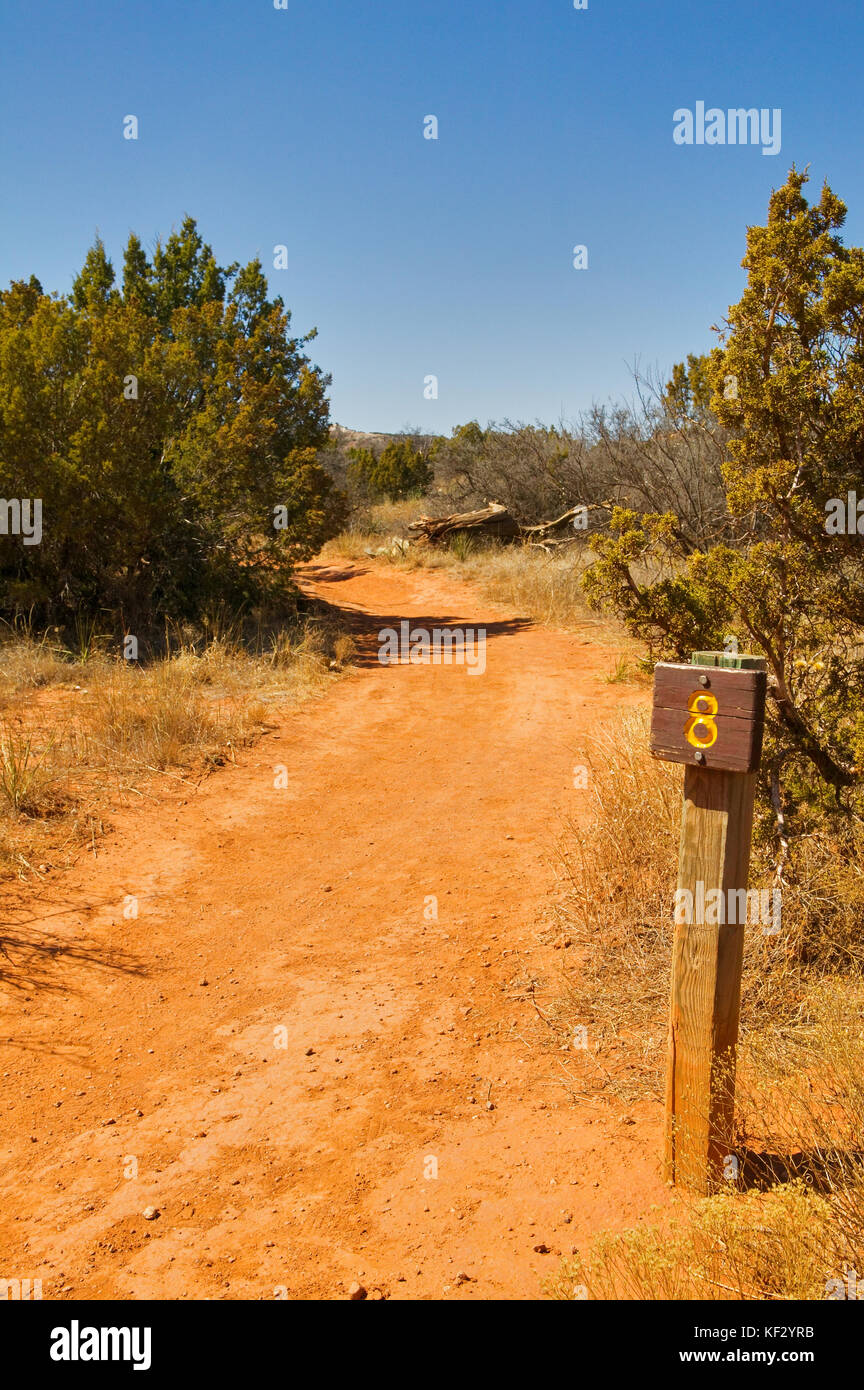 Un rosso secco del deserto sentiero a piedi e il marcatore di distanza segno posto a Palo Duro Canyon, Texas. Foto Stock