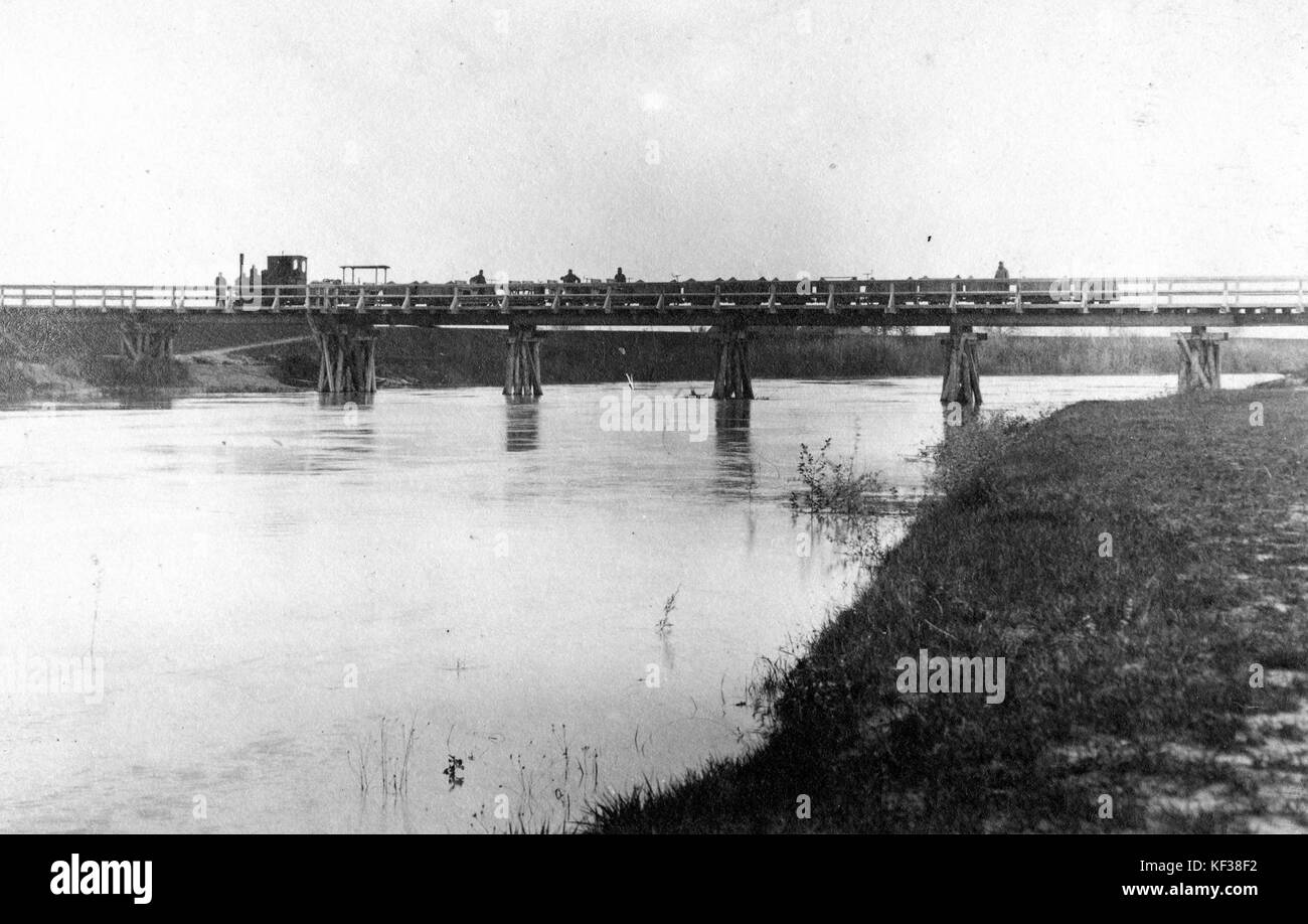 Un'immagine che mostra un fiume con un ponte ferroviario, con una locomotiva a vapore che attraversa un ponte di legno su una ferrovia a scartamento ridotto. Foto Stock