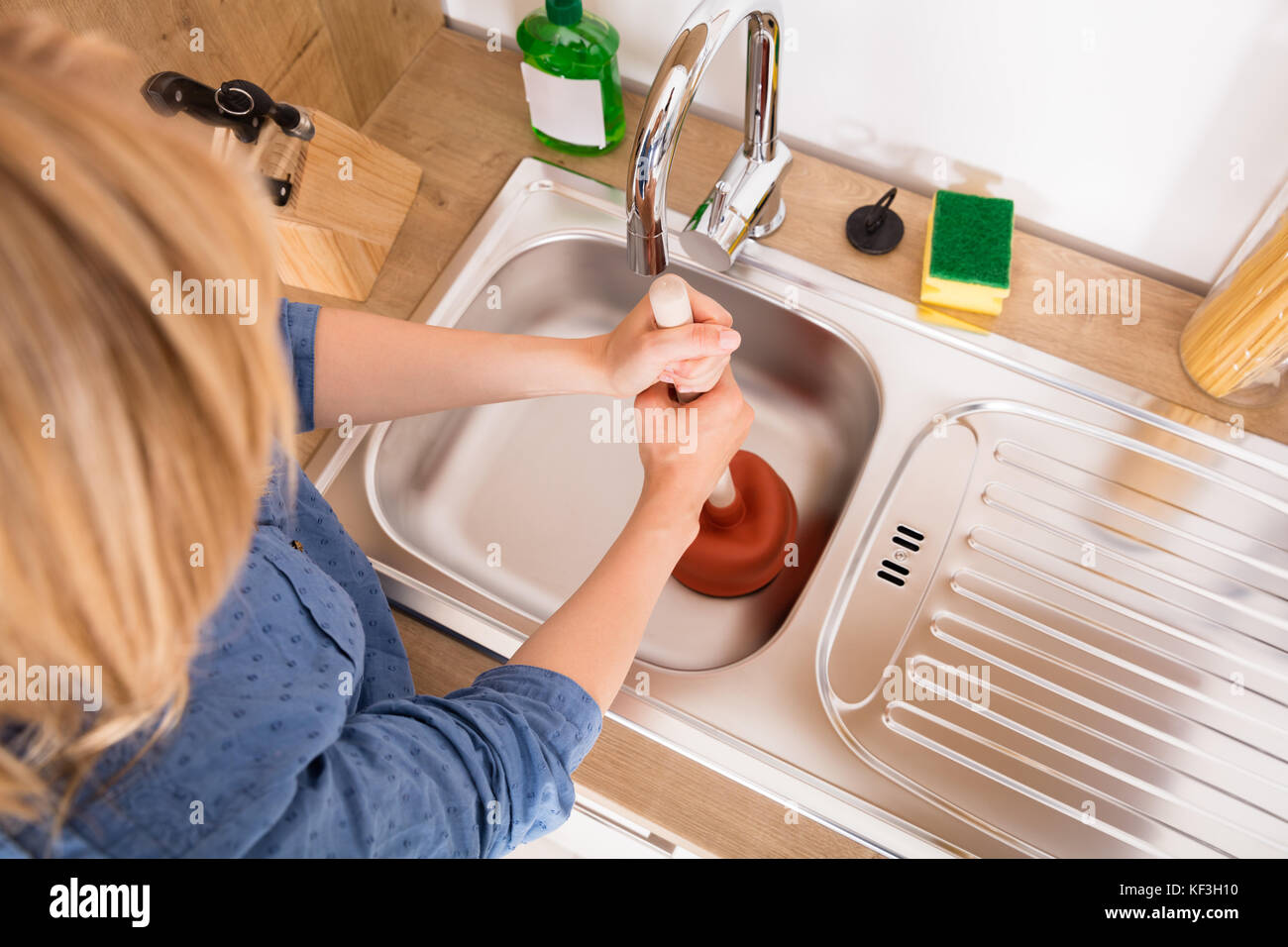 Elevato angolo di visione della donna con pistone bloccato nel lavello da cucina per rimuovere eventuali otturazioni svuotare Foto Stock
