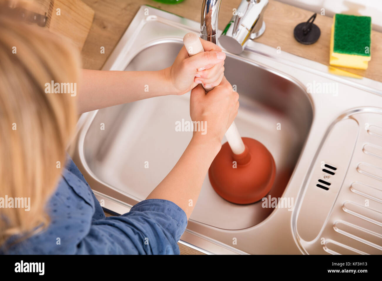Elevato angolo di visione della donna con pistone bloccato nel lavello da cucina per rimuovere eventuali otturazioni svuotare Foto Stock