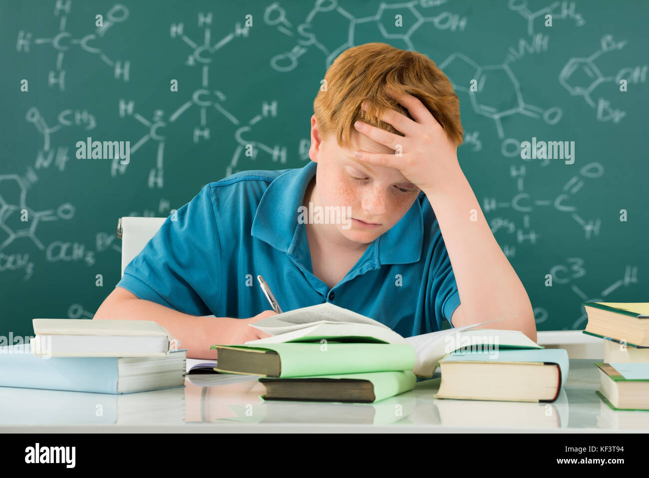 Stanco ragazzo studiare in aula con libri sulla scrivania Foto Stock