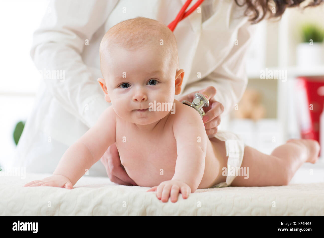 Pediatra esamina neonato ragazzo. medico utilizzando uno stetoscopio per ascoltare il bambino torna il controllo del battito cardiaco. kid sta guardando la telecamera. Foto Stock