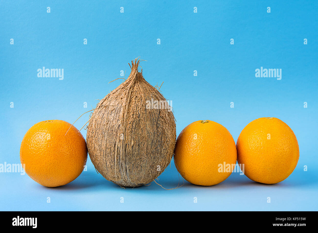 Fila di arance identici una sola noce di cocco su sfondo blu. Individualità personalità concetto di unicità. creative immagine ispiratrice. spazio copia Foto Stock