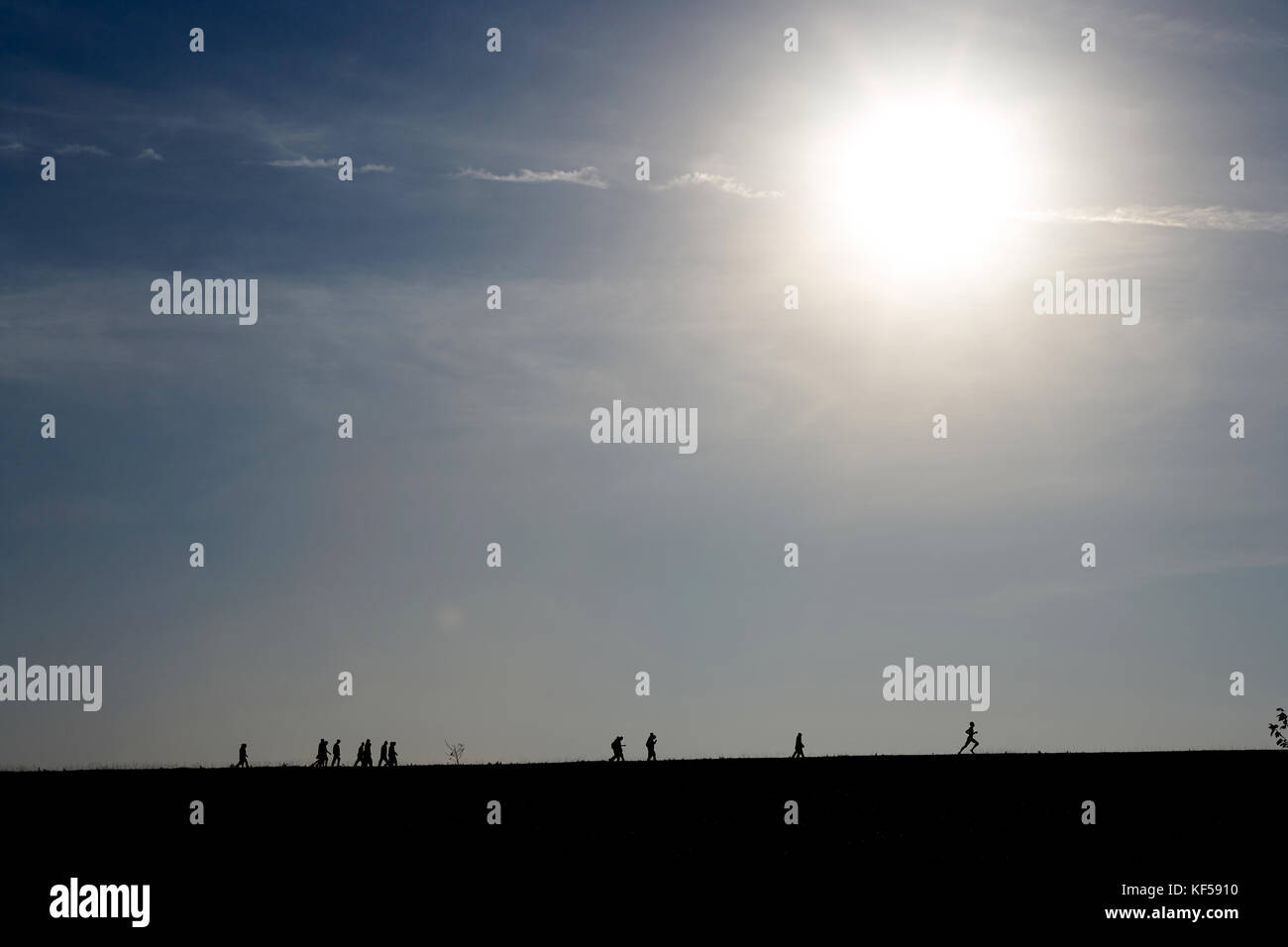 Cercando in un luminoso sunburst con sagome di persone lontane all'orizzonte la corsa e la camminata e spazio di copia su un cielo nebuloso con flare Foto Stock