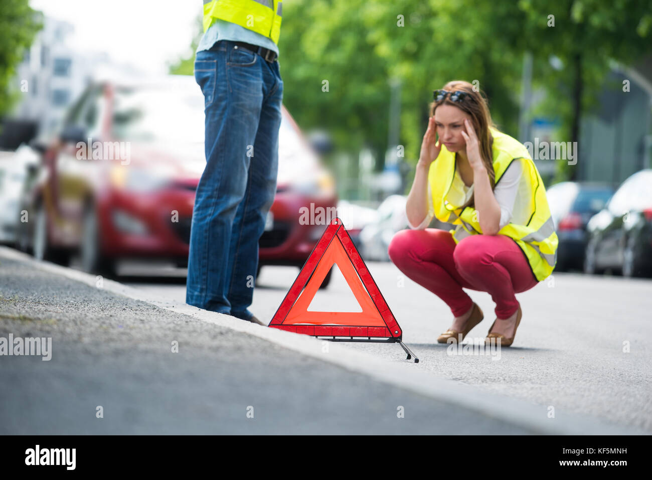 Giovane donna preoccupati accovacciati vicino triangolare segno di avvertimento con ripartiti in auto sulla strada Foto Stock