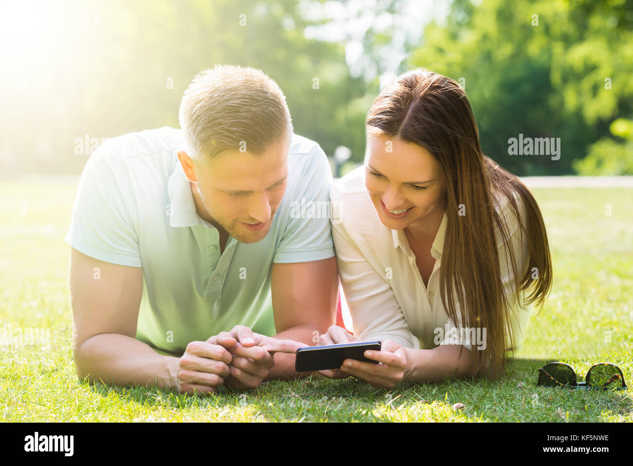 Felice coppia giacendo su erba utilizzando il telefono cellulare Foto Stock