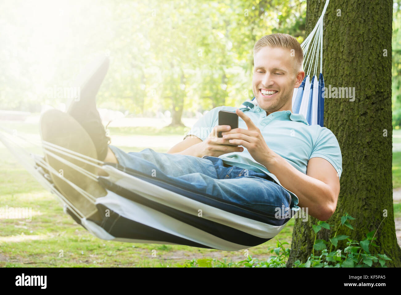Giovane uomo felice utilizzando il telefono cellulare mentre vi rilassate in un amaca in giardino Foto Stock