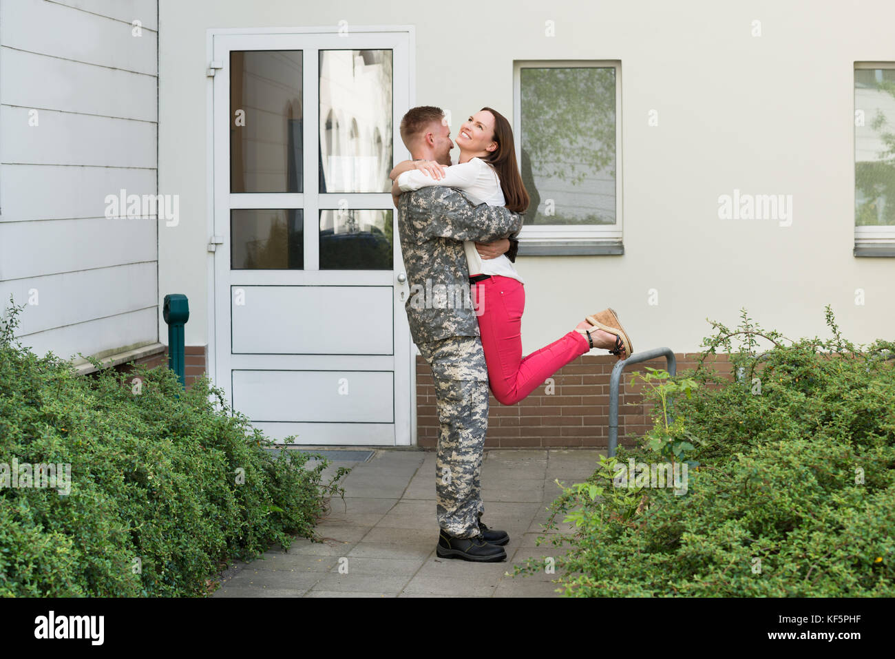 Giovane moglie felice accogliente il marito dal esercito lasciare Foto Stock