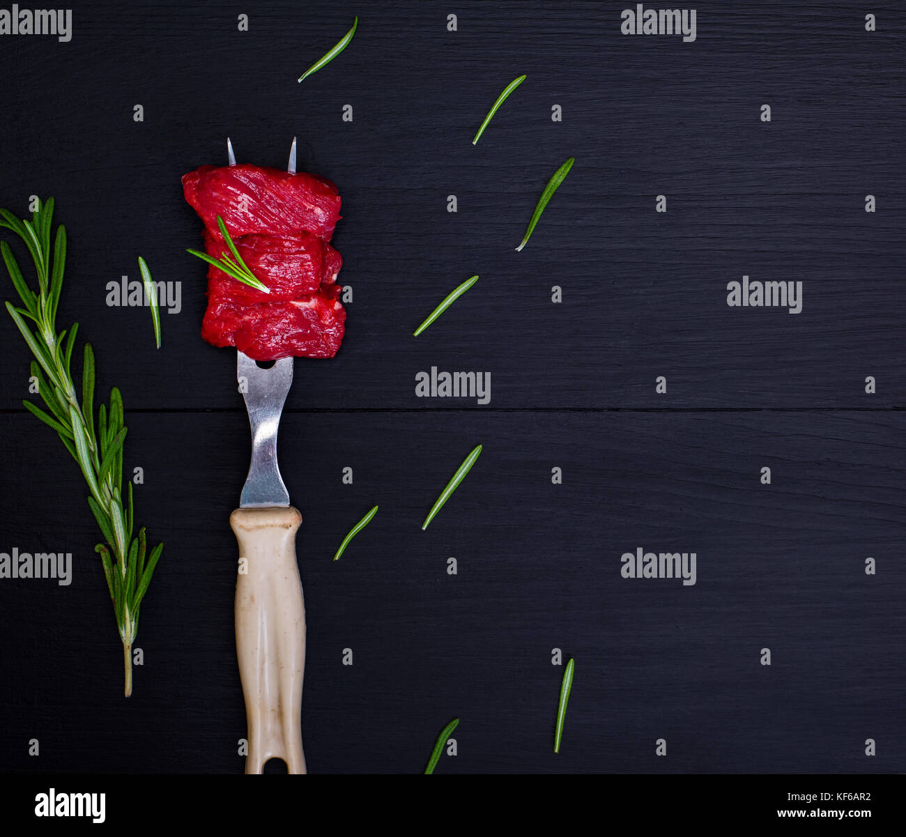 Pezzi di carne di manzo crudo sulla forcella da cucina con manico in plastica su uno sfondo nero, uno spazio vuoto a destra Foto Stock