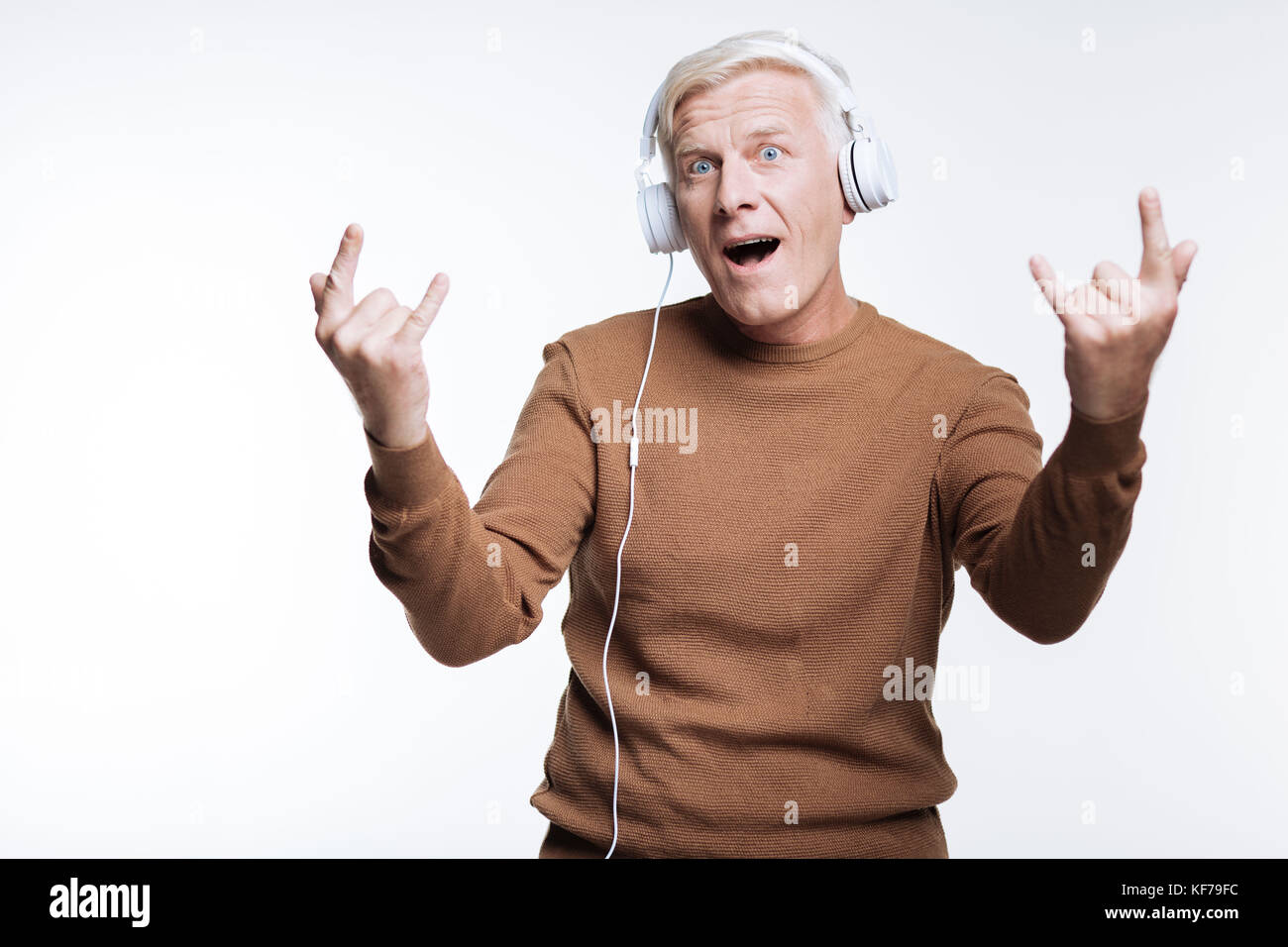 Senior uomo che ascolta musica e che mostra segni di corna Foto Stock