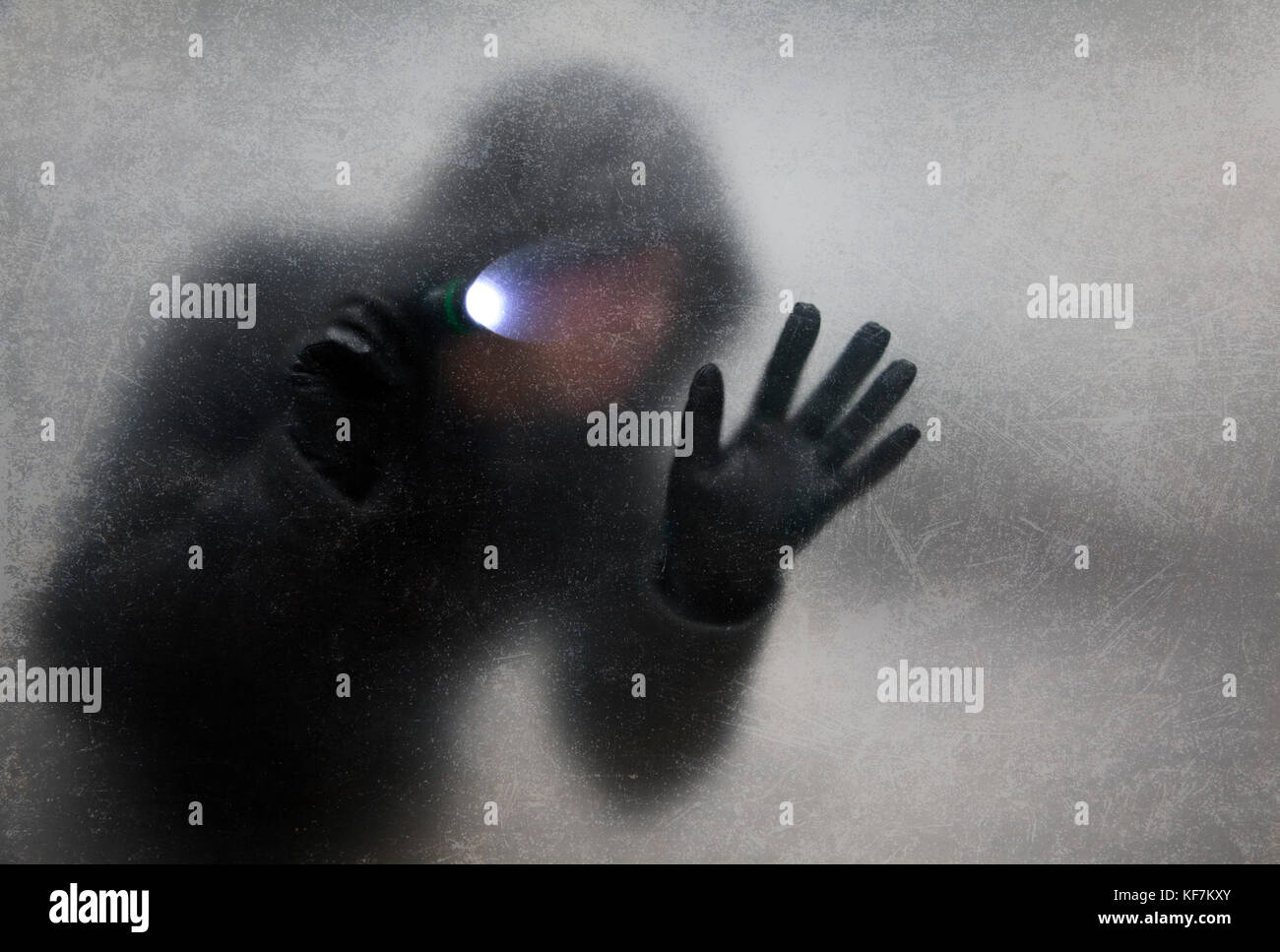 Ladro con torcia dietro un polveroso vetro graffiato Foto Stock