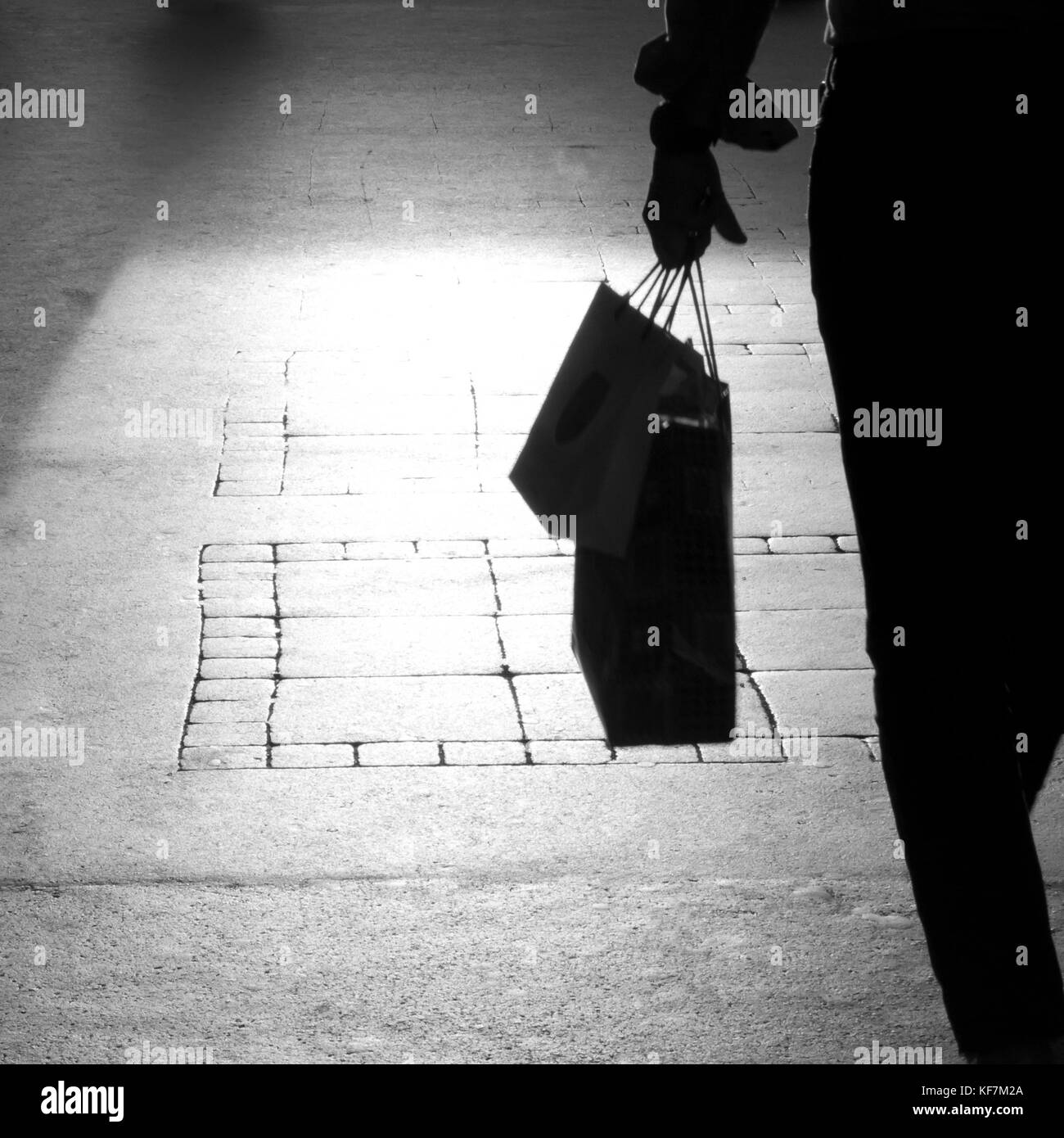 Dettaglio sfocato di una silhouette di un uomo sulla strada di città marciapiede a piedi portante presenta in borse della spesa in mano , in bianco e nero Foto Stock