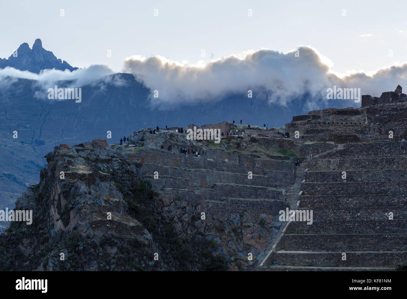 La gente che camminava sulle terrazze del pumatallis, antica fortezza inca e montagne coperte di nuvole, Valle Sacra, Ollantaytambo, Perù Foto Stock
