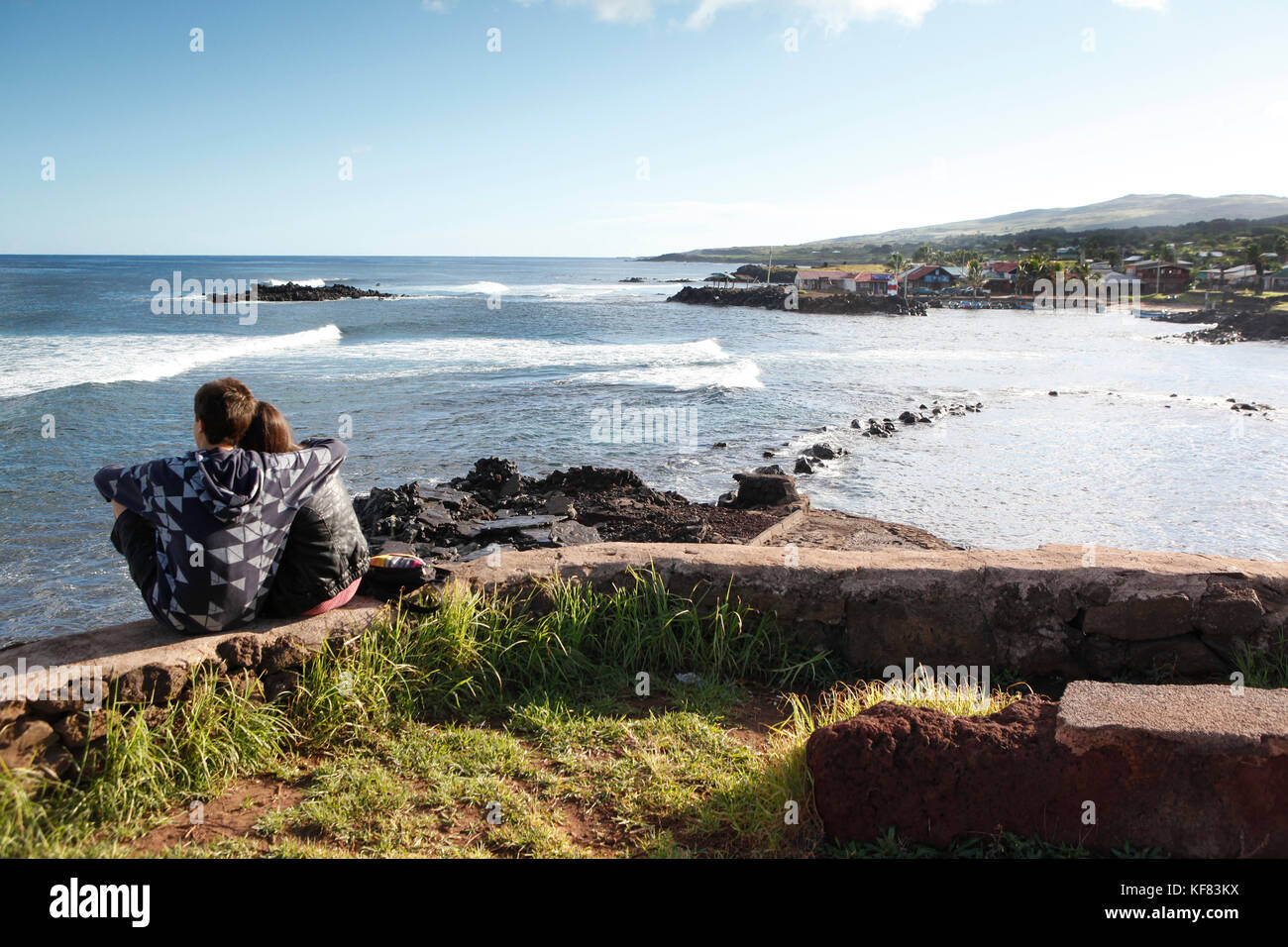Isola di Pasqua, Cile, Isla de Pascua, Rapa Nui, un giovane si siede e orologi surf venite nel vicino a Hanga Roa Foto Stock