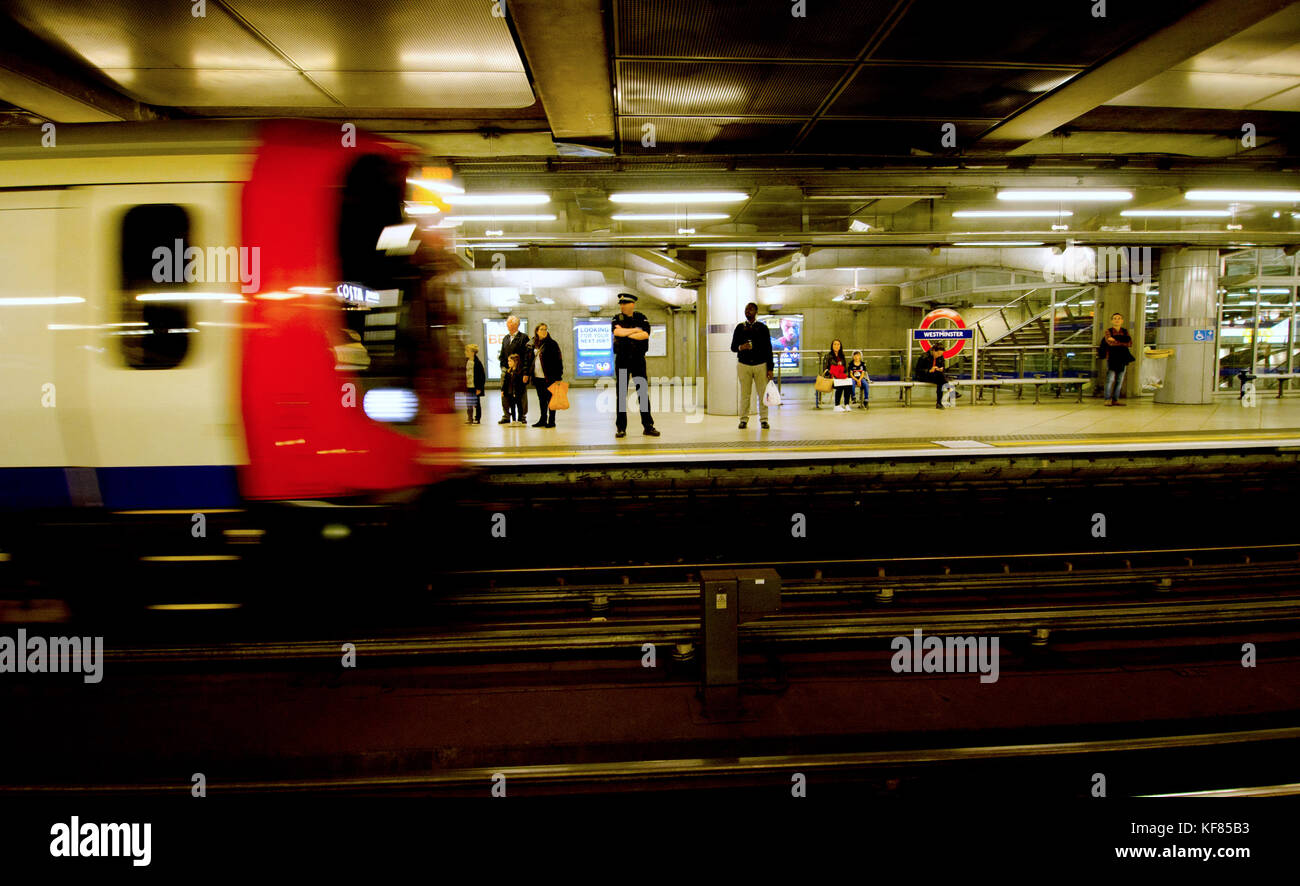 Londra, Inghilterra, Regno Unito. Funzionario di polizia sulla piattaforma di Westminster stazione della metropolitana come un treno arriva Foto Stock