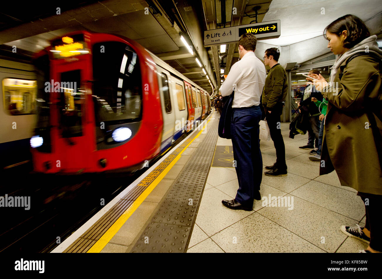 Londra, Inghilterra, Regno Unito. Persone sulla piattaforma di Westminster stazione della metropolitana come un treno arriva Foto Stock