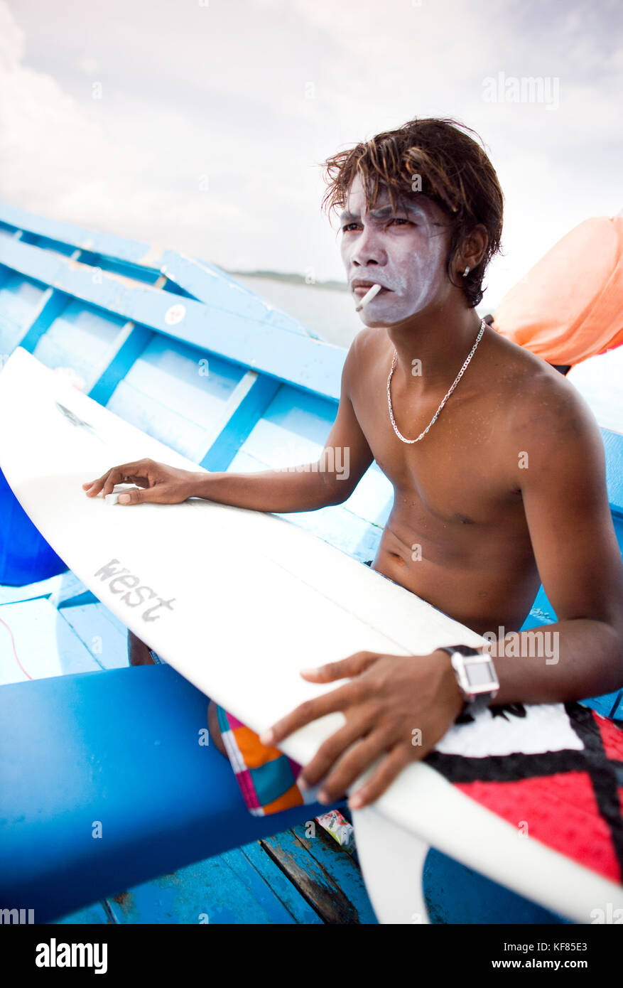 INDONESIA, Isole Mentawai, Kandui Surf Resort, giovane uomo con crema solare  sul viso, fumando e tenendo la sua tavola da surf Foto stock - Alamy