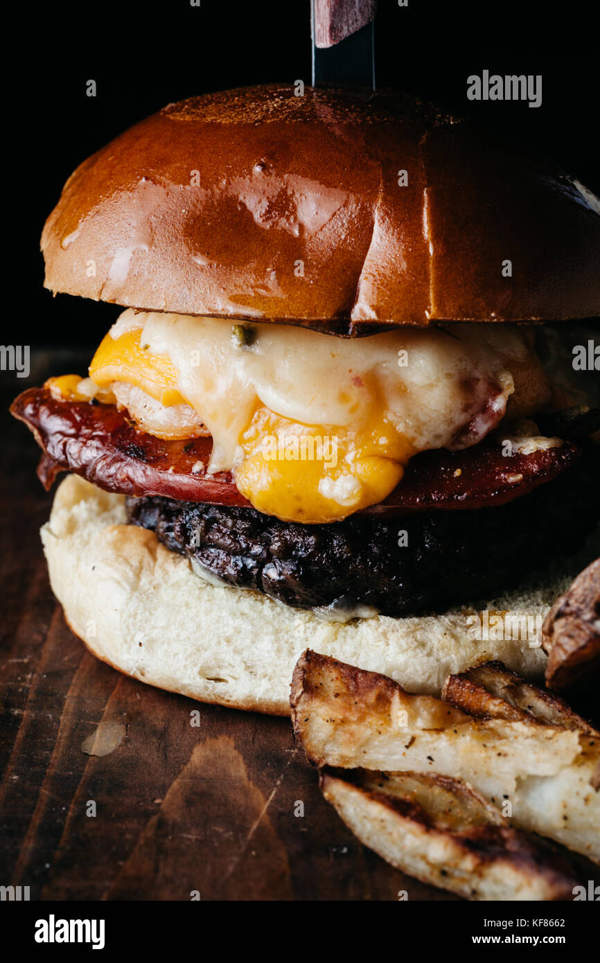 Giganic burger con chorizo e un uovo fritto servito con patate fritte su scuro dello sfondo rustico Foto Stock