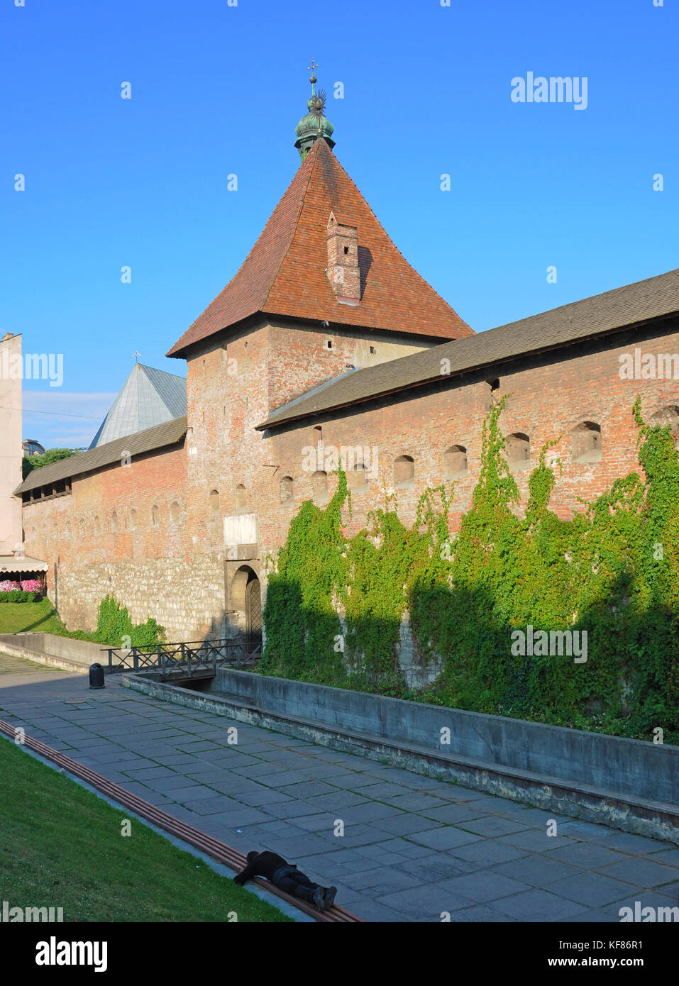 Parete della città con una torre e una persona che dorme su una panchina al di fuori Foto Stock