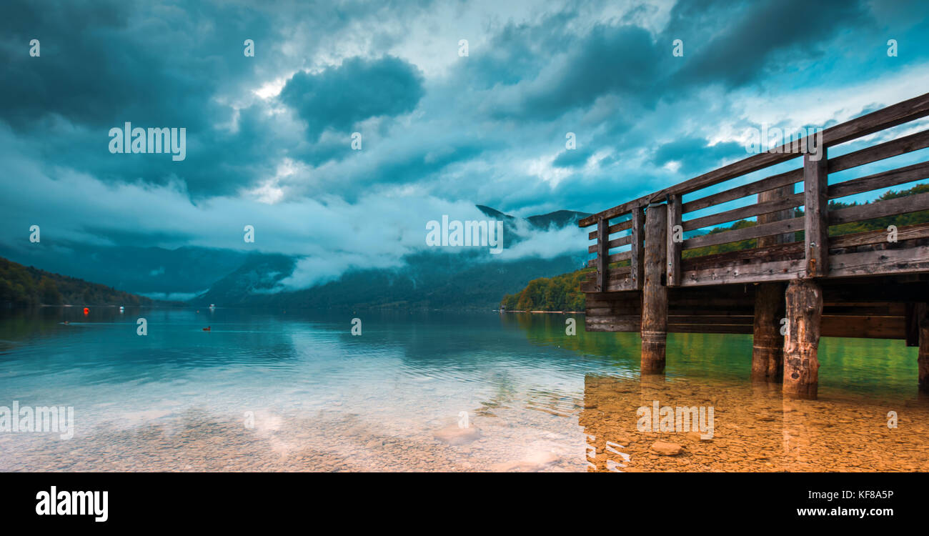 Il molo di legno al bellissimo lago di Bohinj paesaggio su nuvoloso giornata autunnale. Unico lago glaciale in sloveno parco nazionale del Tricorno. Foto Stock