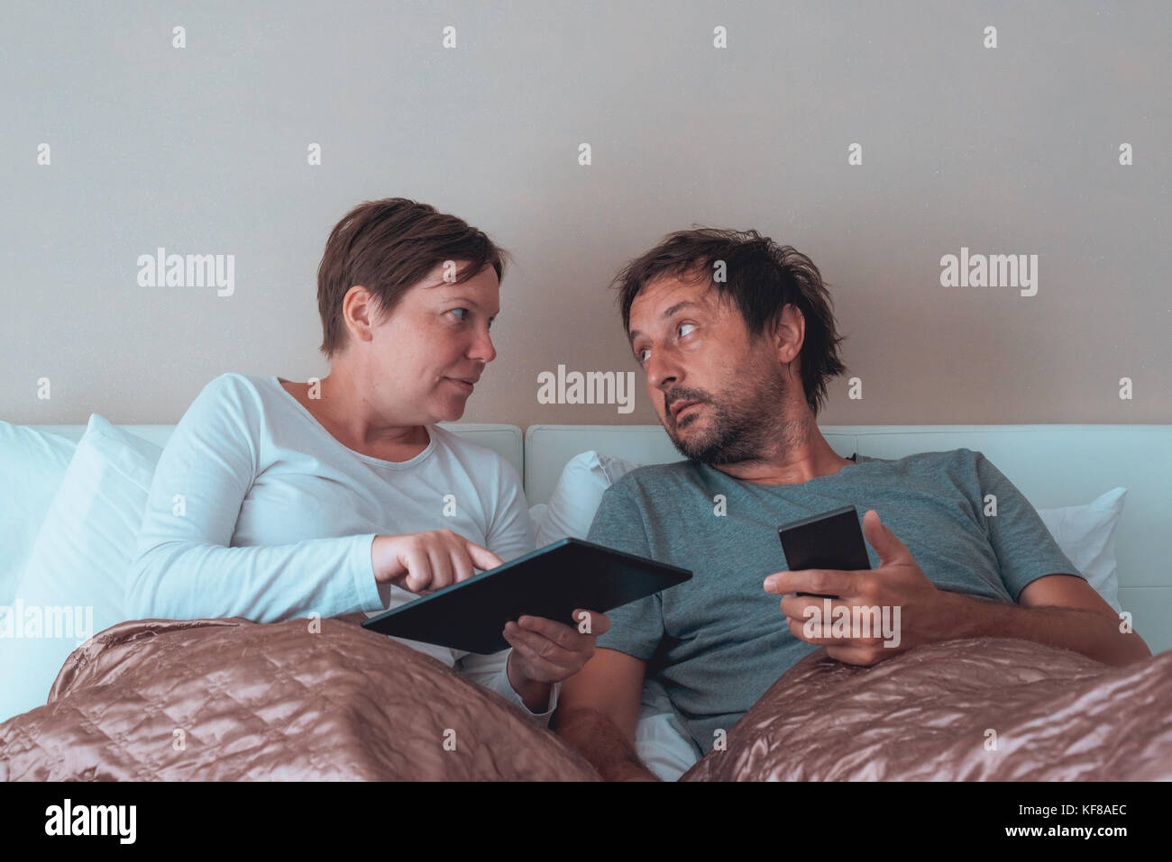 Grave giovane, il marito e la moglie in camera da letto utilizzando dispositivi elettronici personali Foto Stock