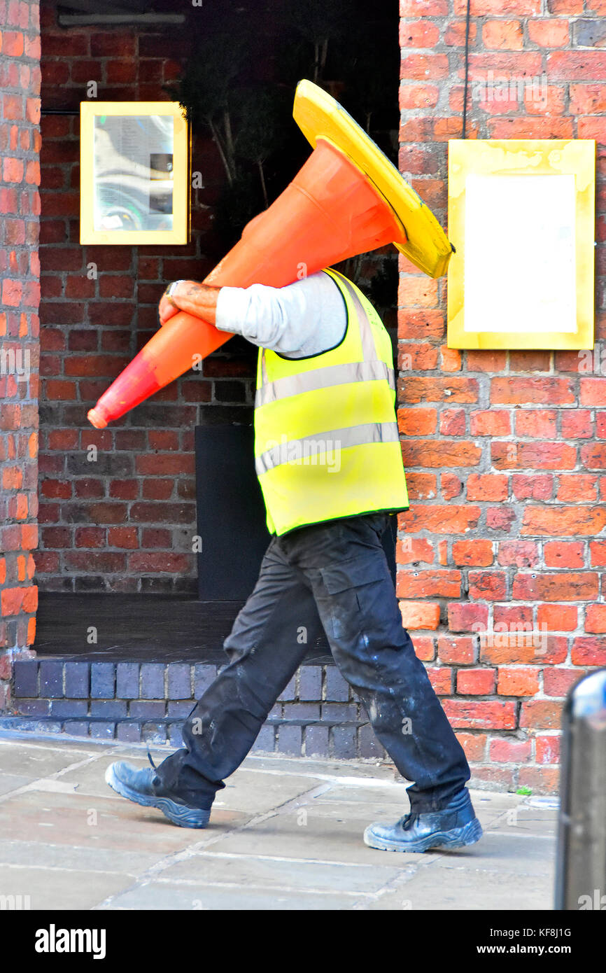 Uomo al lavoro camminando lungo il marciapiede in Liverpool indossando GIUBBETTO ALTA VISIBILITA portando un grande cono stradale bollard sulla sua spalla England Regno Unito Foto Stock