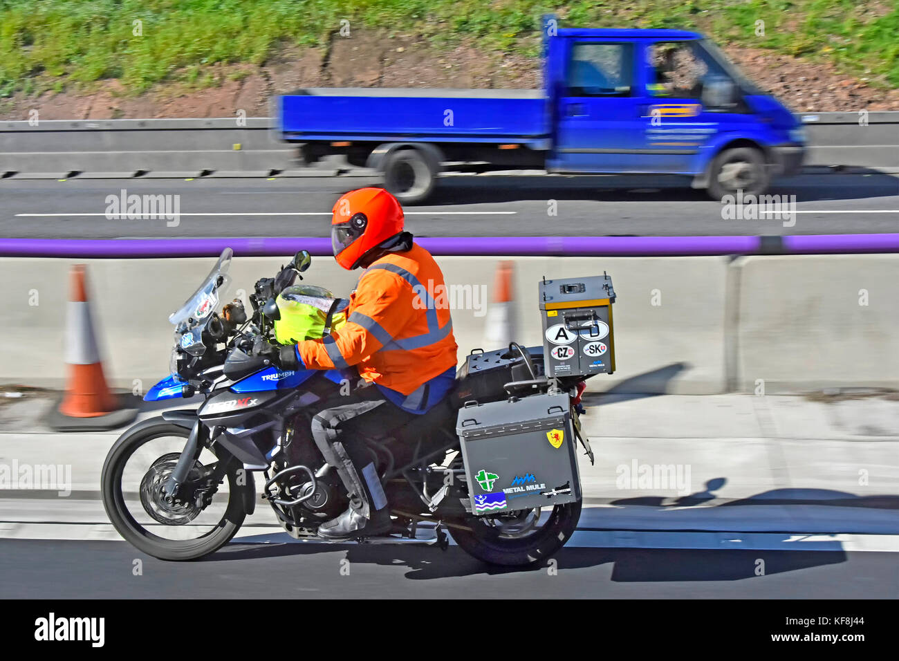 Close up di Triumph Motor bike rider guidando lungo tre corsie di autostrada UK indossando alta vis giacca e casco in opere stradali sezione Foto Stock