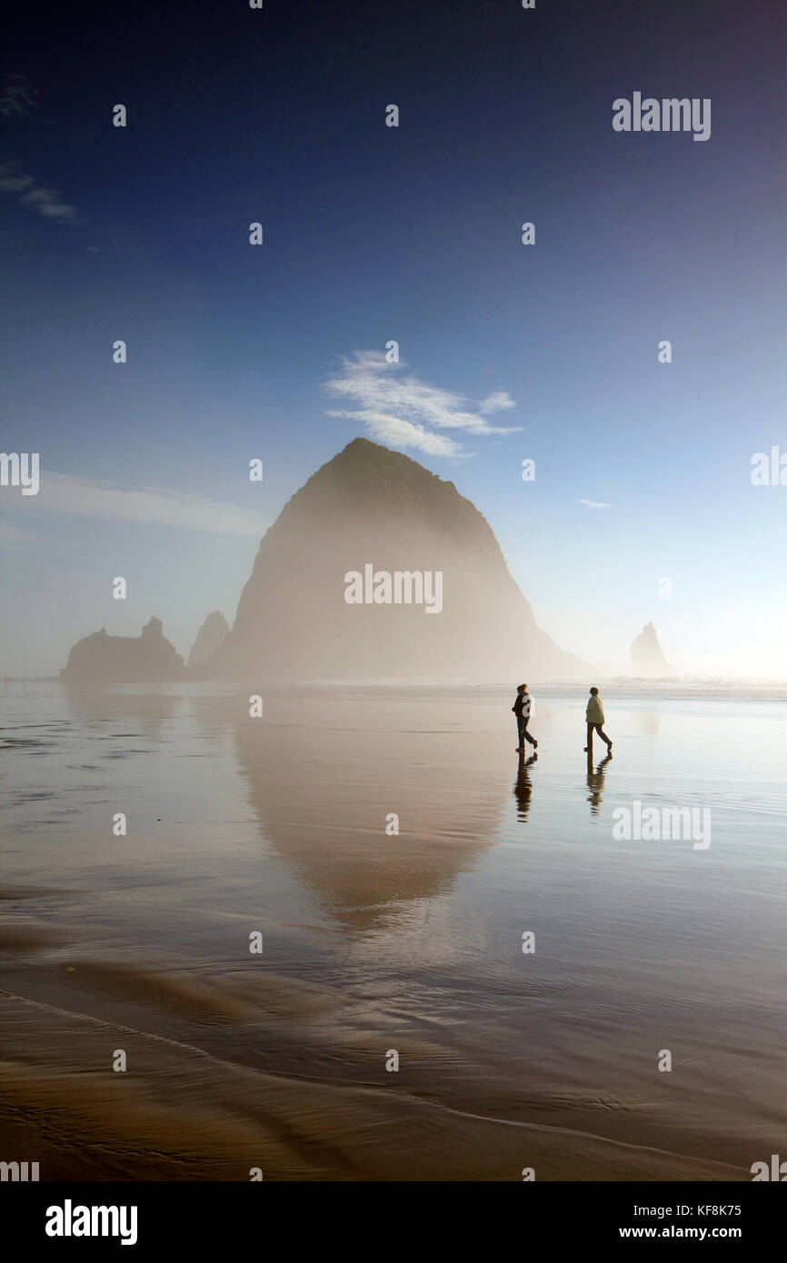 Stati Uniti d'America, oregon, città del pacifico, individui a piedi lungo la Pacific city beach con haystack rock a distanza Foto Stock