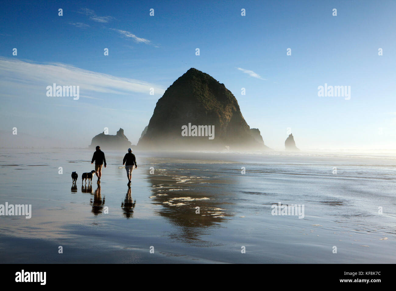 Stati Uniti d'America, oregon, città del pacifico, individui a piedi lungo la Pacific city beach con haystack rock a distanza Foto Stock