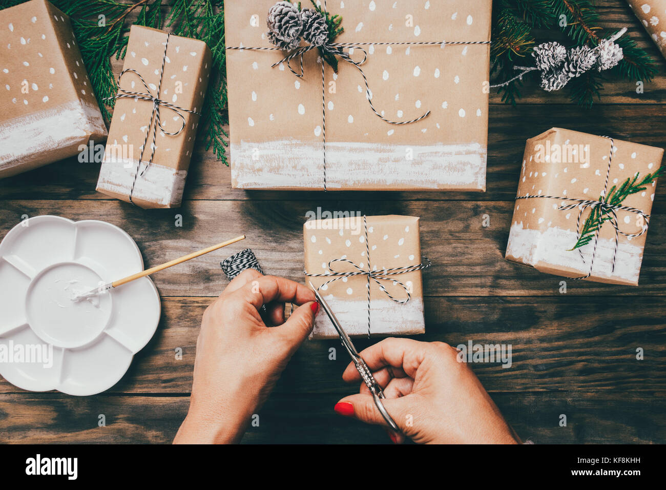Regali Di Natale In Legno.Donna Di Mani Impacchettare I Regali Di Natale Su Carta Marrone Dipinto Con Neve Abete Rami E Pigne Nelle Quali Su Un Rustico Di Legno Vista Superiore Foto Stock Alamy