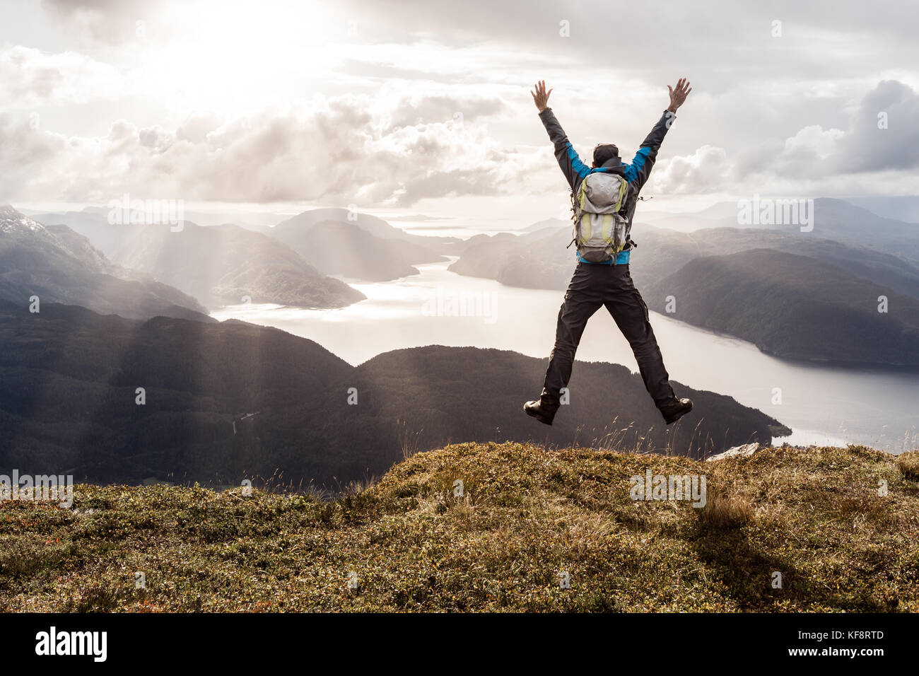 L'uomo raggiungendo il culmine e saltando di gioia. splendida vista alle montagne costiere e fiordi. hellandsnuten, sandsfjord, Norvegia. Foto Stock