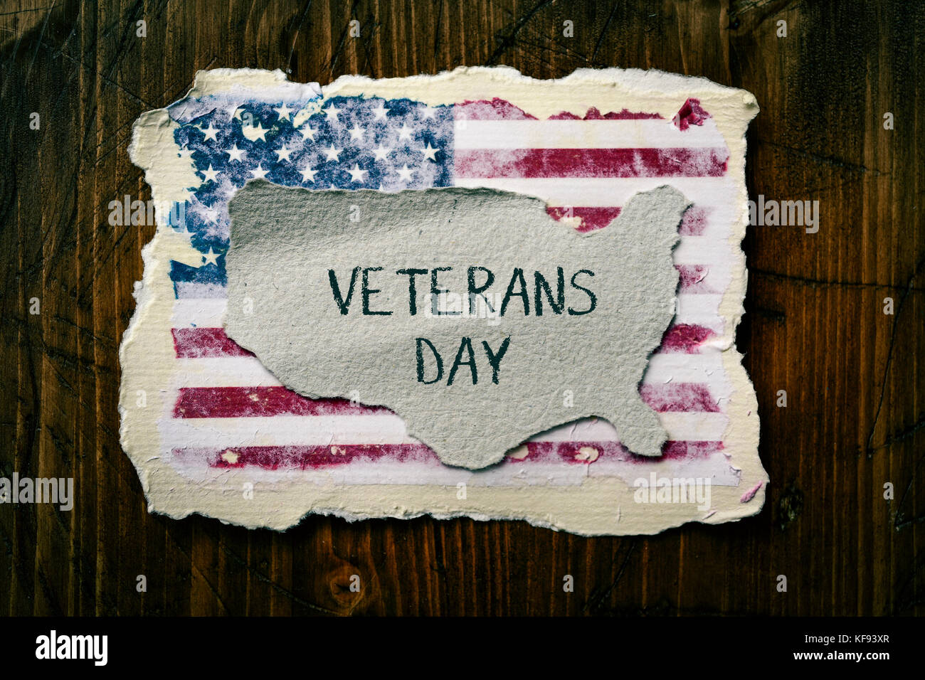 Foto ad alto angolo di un pezzo di carta a forma di Stati Uniti con il testo veterani giorno scritto in esso e una bandiera degli Stati Uniti, su un legno rustico Foto Stock