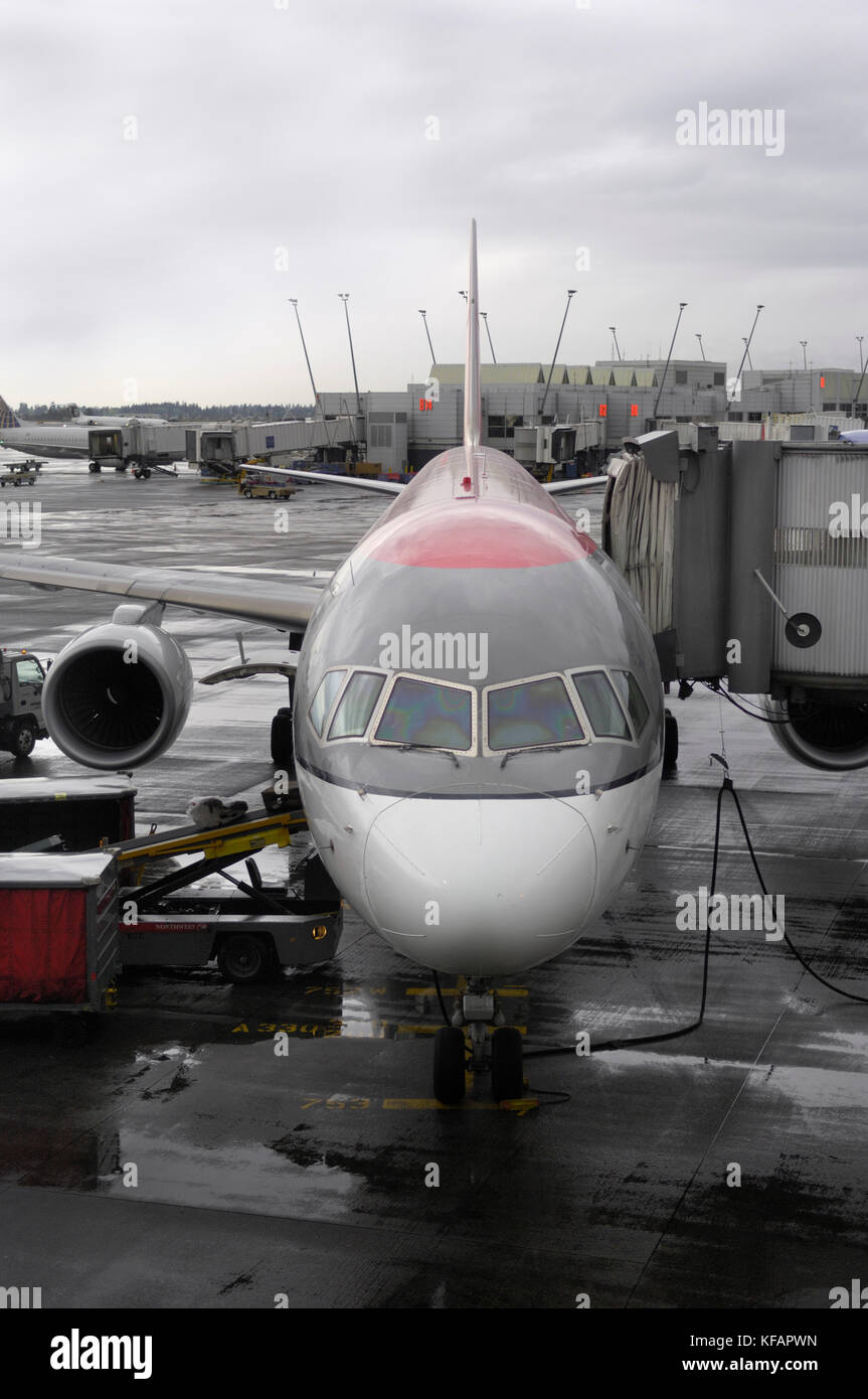 Sottocarro nosewheel, parabrezza e motore di Northwest Airlines Boeing 757-300 parcheggiato con jetway estesa su un grembiule umido, sacchi su un bagaglio essere Foto Stock