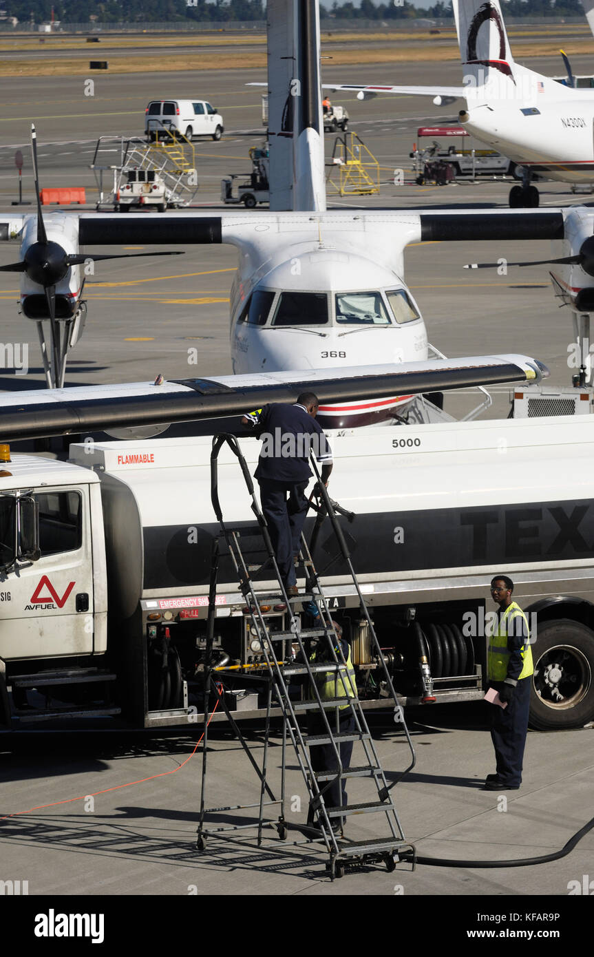 Autofornitori e carrello con un orizzonte aria Bombardier DHC-8 Dash 8-200 parcheggiata e tail-pinna di un DHC-8 Dash 8-400 Q400 dietro Foto Stock