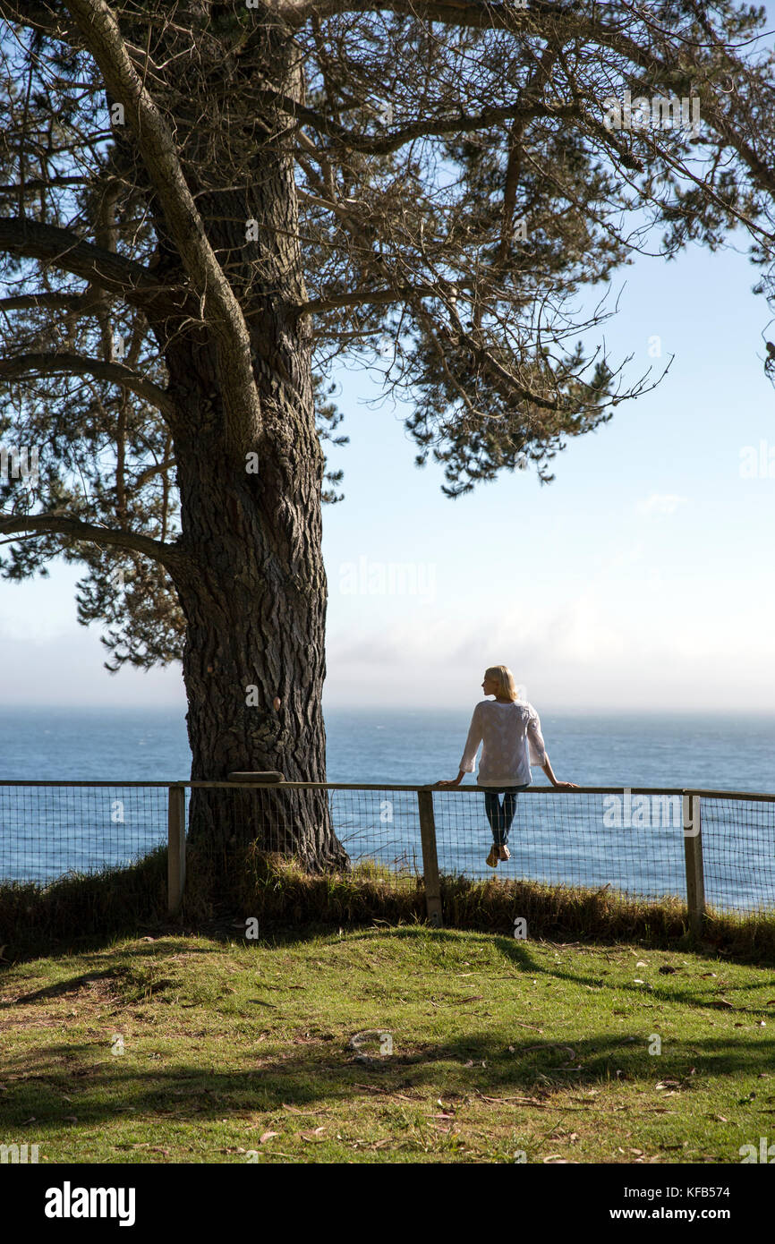 Stati Uniti, California, Big Sur, esalen, donna siede sul recinto vicino alla fattoria e gode del sole e la vista dell'oceano pacifico, il Esalen Institute Foto Stock