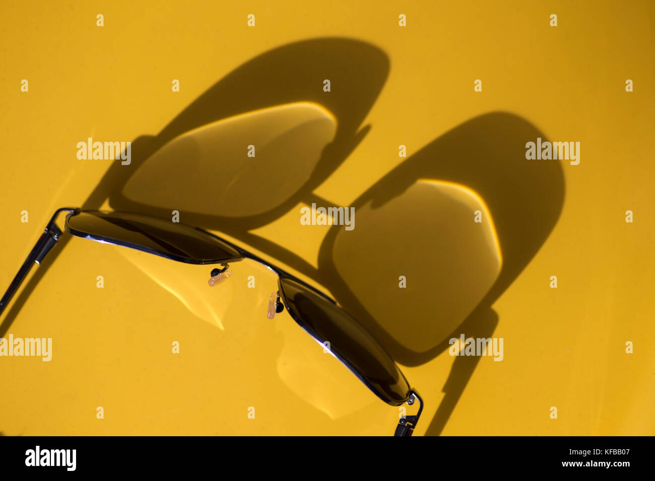 Vista astratta delle ombre proiettate dalla luce del sole su uno sfondo giallo di un paio di occhiali da vista Foto Stock