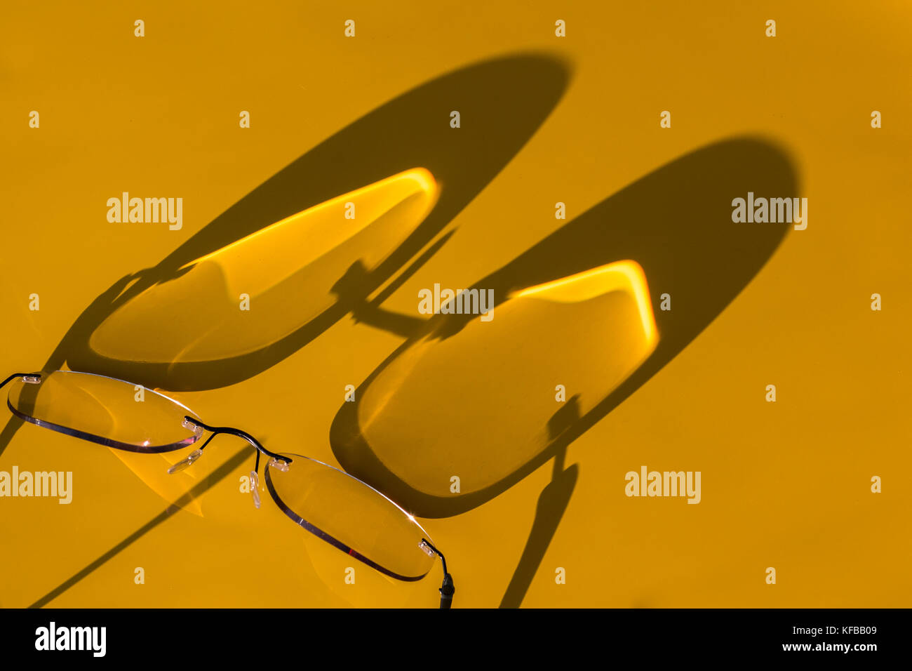 Vista astratta di ombre proiettate dalla luce del sole su uno sfondo giallo di un paio di occhiali Foto Stock