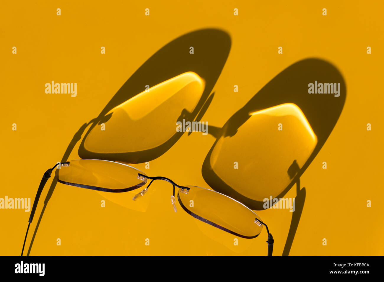Vista astratta delle ombre proiettate dalla luce del sole su uno sfondo giallo di un paio di occhiali da vista Foto Stock