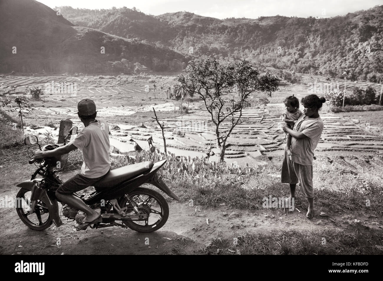 Indonesia, Flores, le persone si radunano sul ciglio della strada con vista di una valle ricca di campi di riso e i lavoratori a distanza, waturaka village Foto Stock