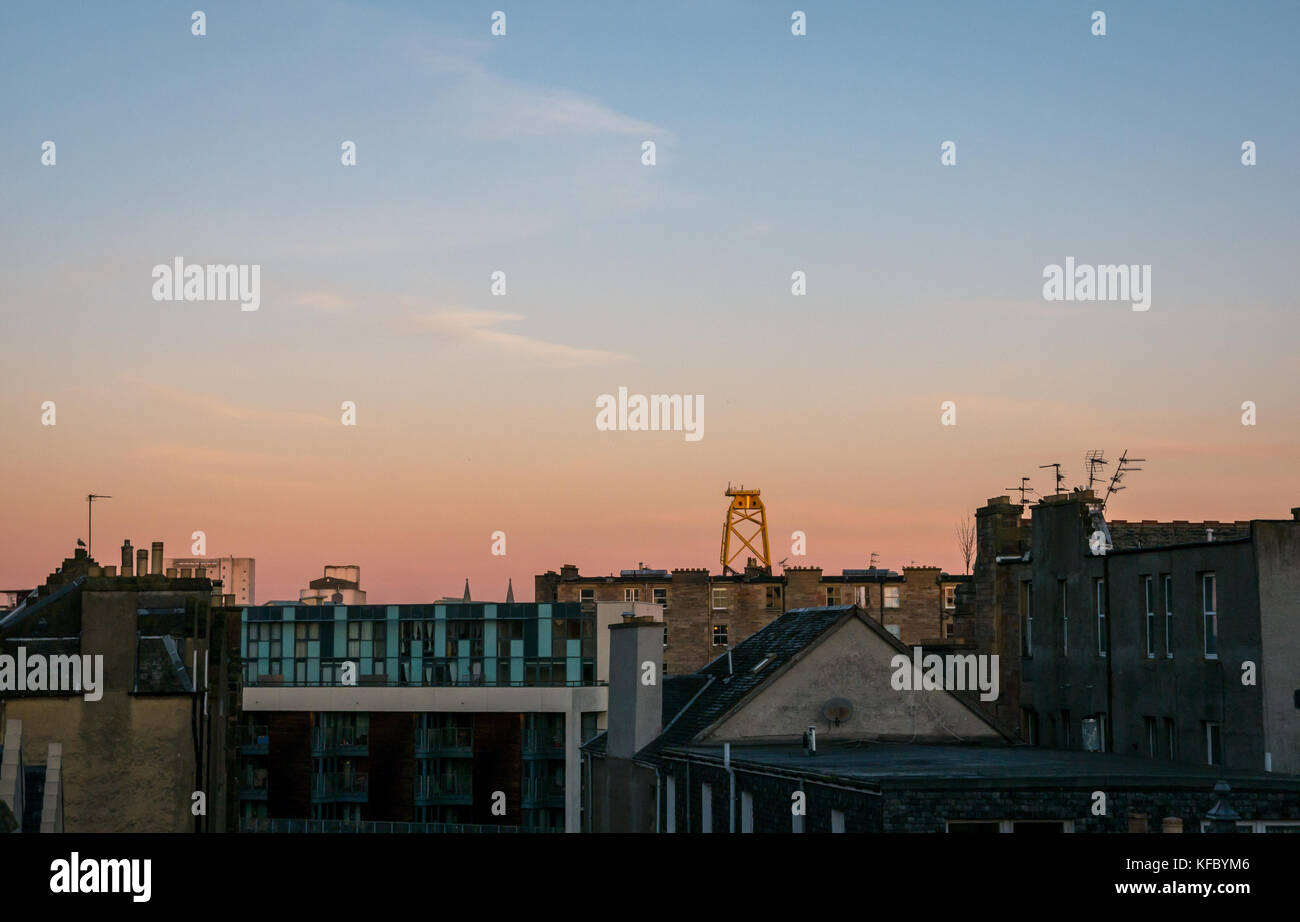 Leith, Edimburgo, Scozia, Regno Unito. La mattina presto sunrise su Leith tetti con alba di colori e di un enorme turbina eolica piattaforma ormeggiata in Leith Dock bacino ingresso torreggianti sull'orizzonte in distanza Foto Stock