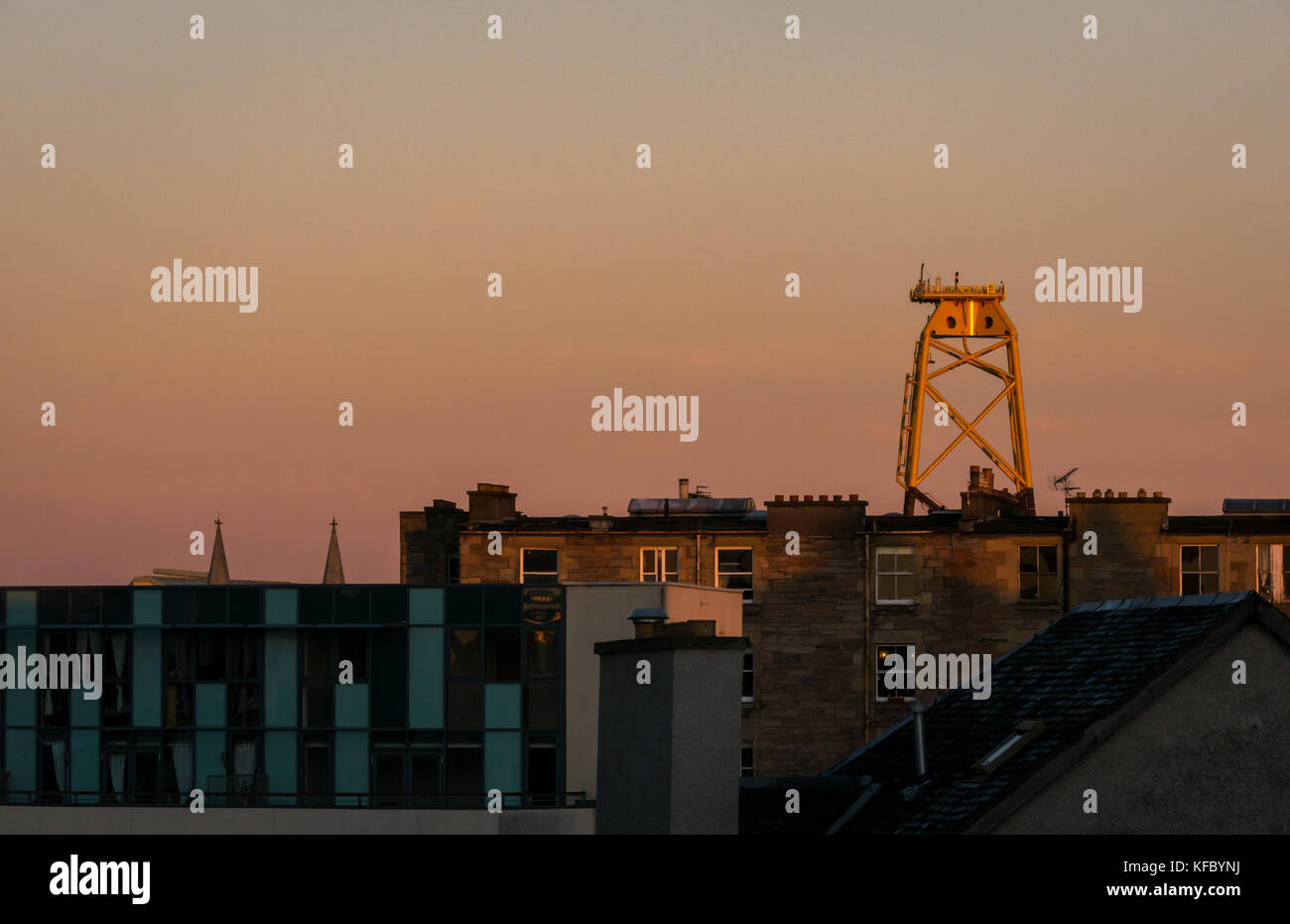 Leith, Edimburgo, Scozia, Regno Unito. Alba di mattina presto sui tetti di Leith con i colori dell'alba nel cielo e una piattaforma enorme della turbina del vento ormeggiata nel molo di Leith che torreggia sopra un blocco moderno degli appartamenti Foto Stock