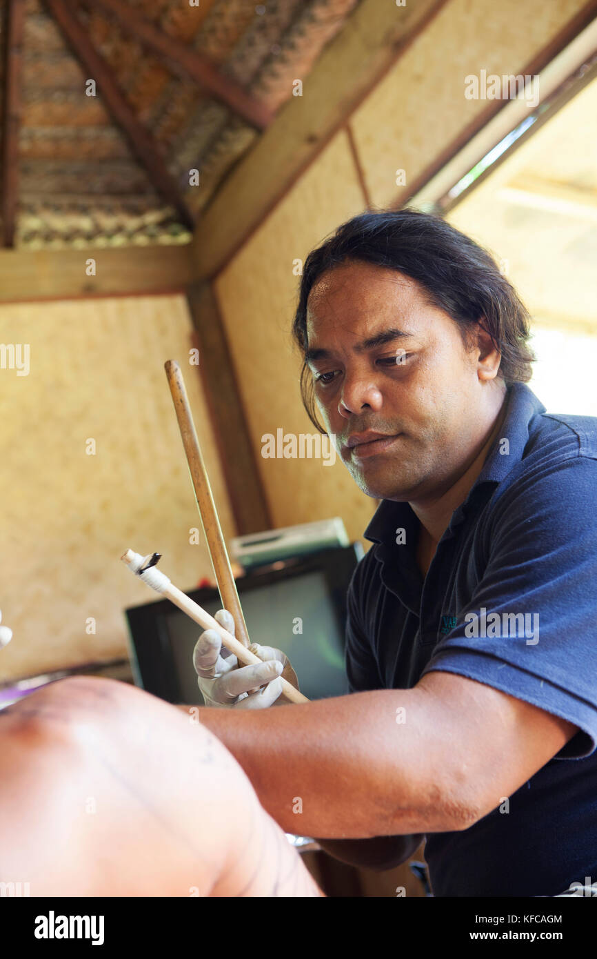 Polinesia Francese, Moorea. James Samuela, un tatuaggio artista applicando un tatuaggio tradizionale sul client nel suo studio nell'Isola di Moorea. Foto Stock