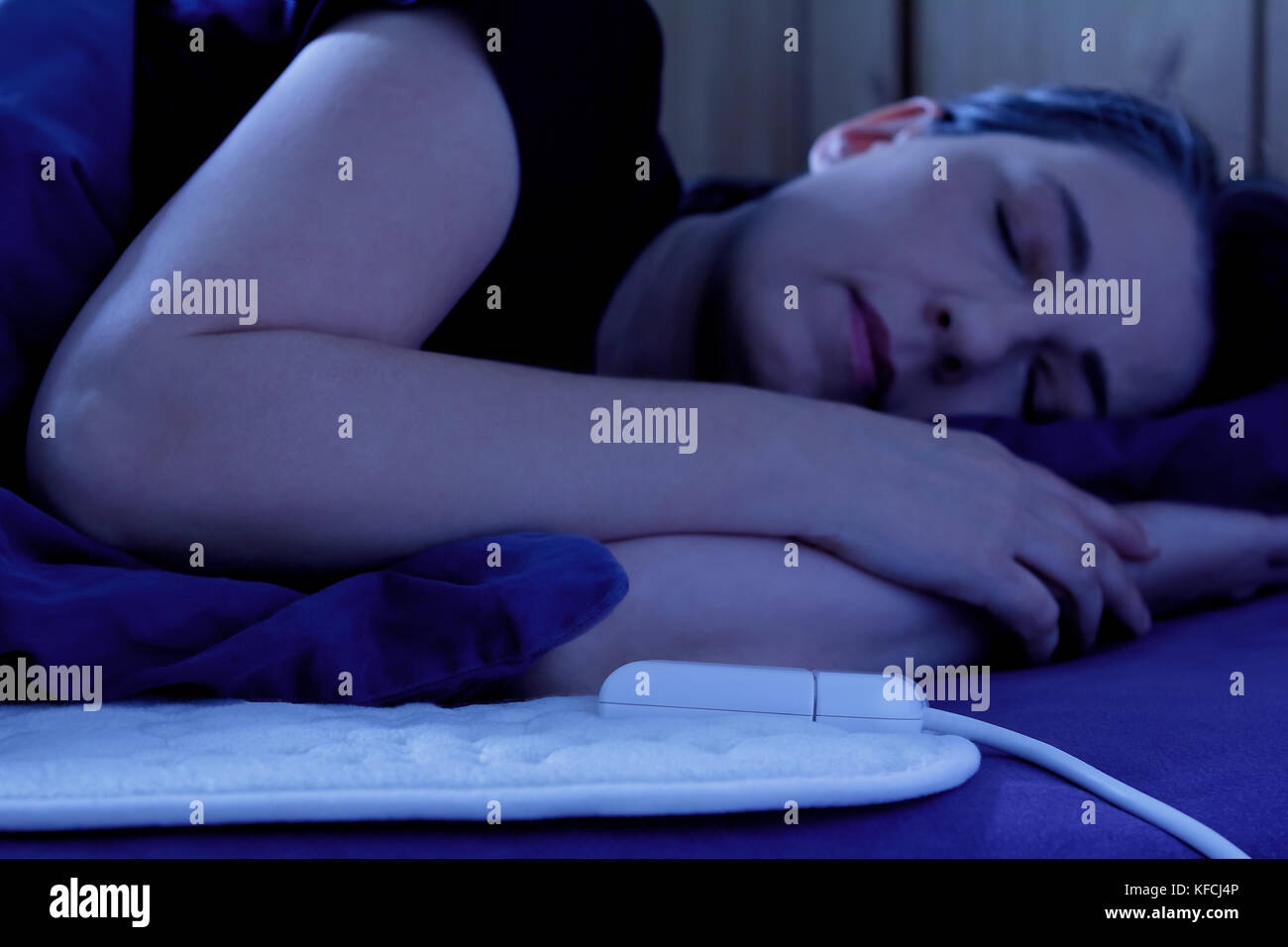 Donna che dorme tranquillamente a riscaldamento elettrico coperta nel suo letto di notte Foto Stock