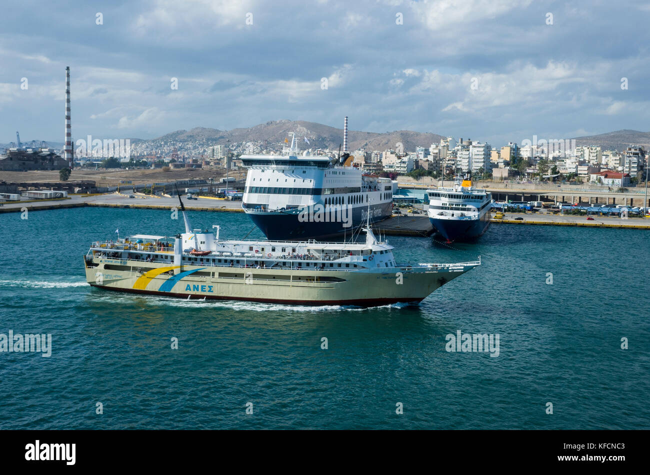 Porto del Pireo di Atene. La Grecia. Una vista in tutta l'acqua verso il dock sull'altro lato del porto. Una nave che entrano in porto. Si tratta di un luminoso Nuvoloso Giorno. Foto Stock