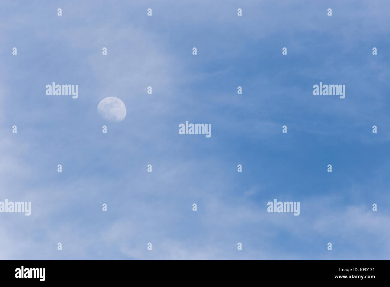 Vista la luna attraverso alcune nuvole nel cielo blu Foto Stock