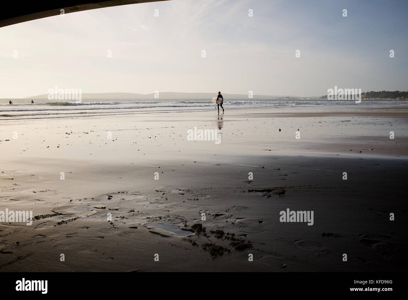 Un surfista camminare sulla spiaggia verso il mare Foto Stock