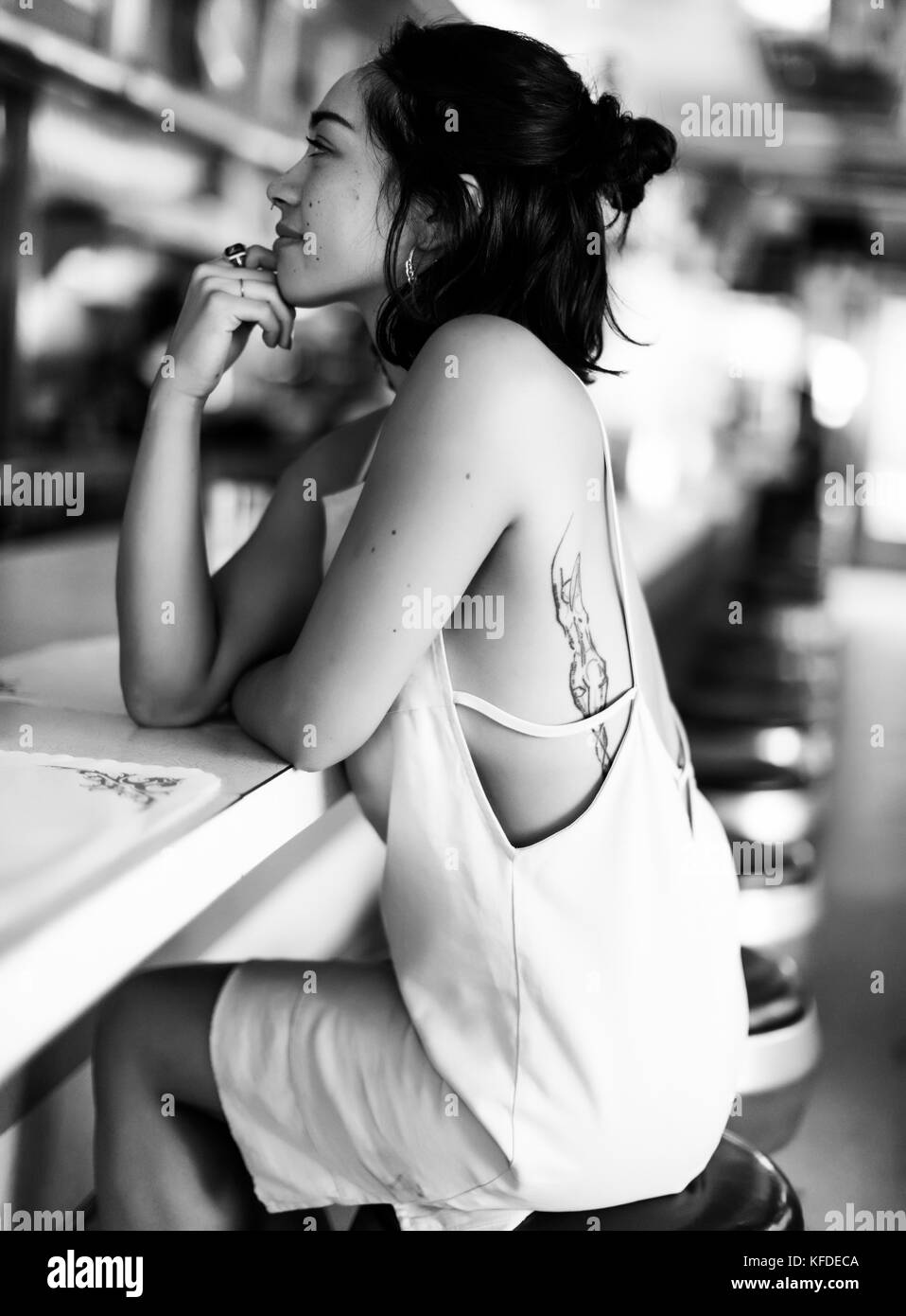 Giovane donna seduta su uno sgabello in corrispondenza di un banco di bar in un diner, mano sul mento. Foto Stock