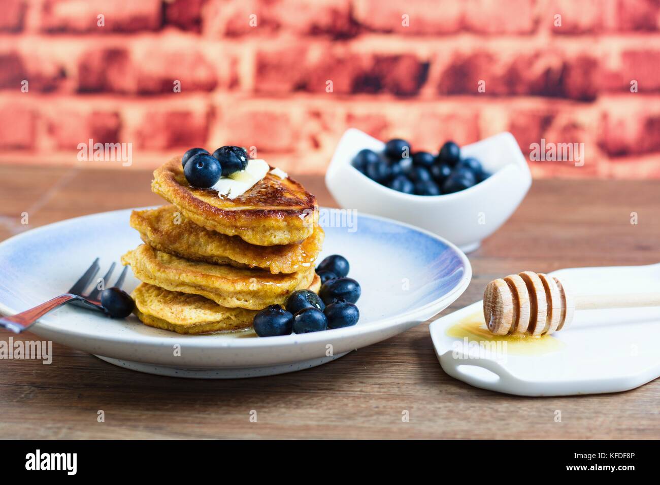 In casa senza glutine pancake con mirtilli, burro e miele di fronte a un muro di mattoni sfondo Foto Stock